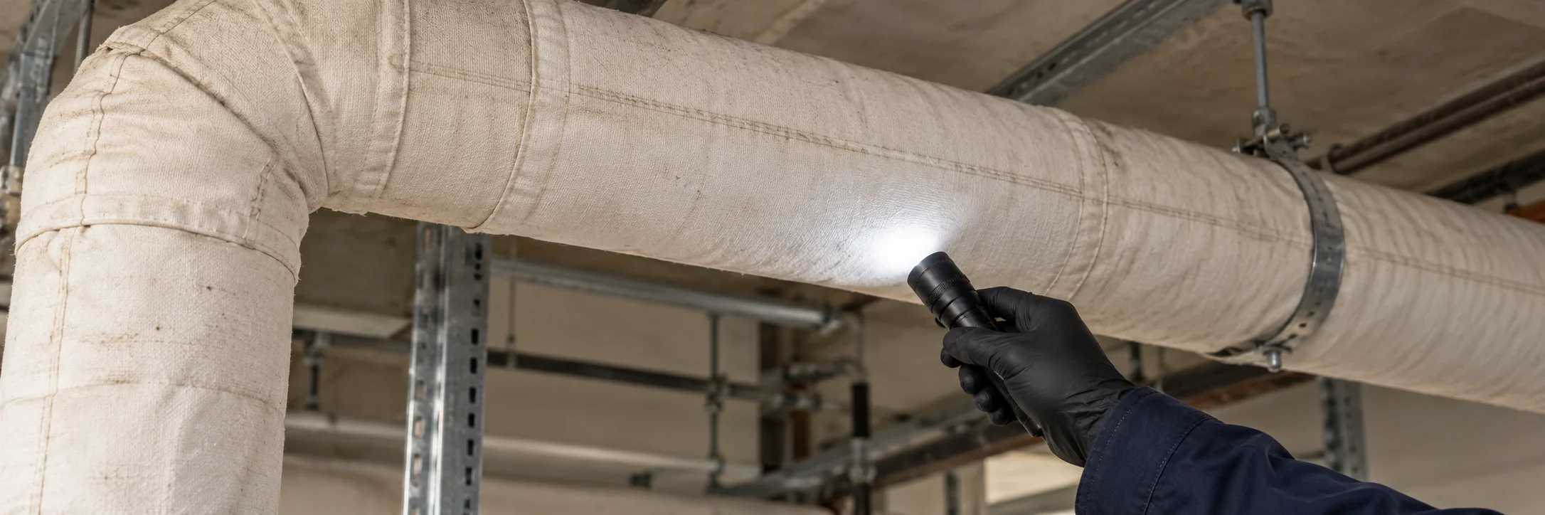 Gloved hand illuminating intact pipe insulation during a building-material survey